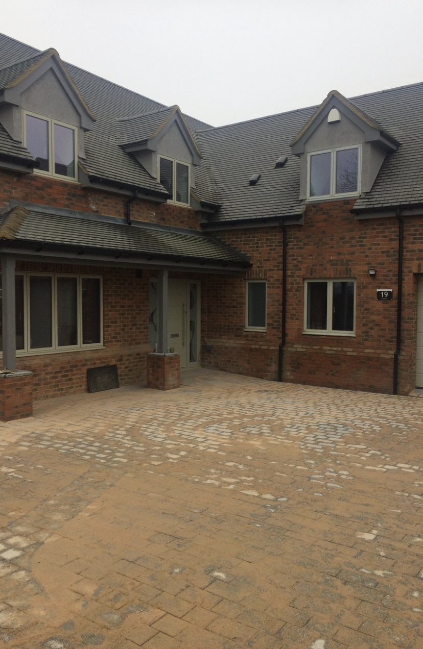 Front of a brick new build with dormers and a block-paved courtyard